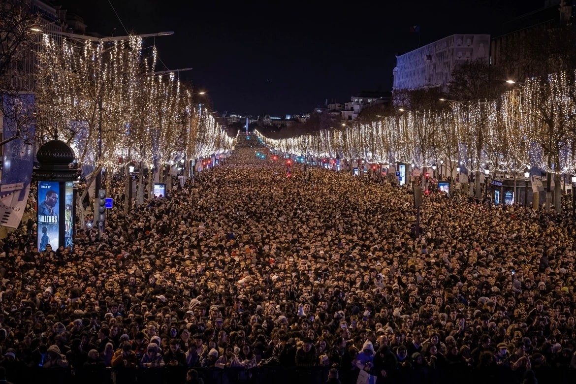 Revellers watch a sound and light show projected on the Arc de Triomphe as they celebrate the New Year on the Champs-Elysees in Paris, France. [Aurelien Morissard/AP Photo]