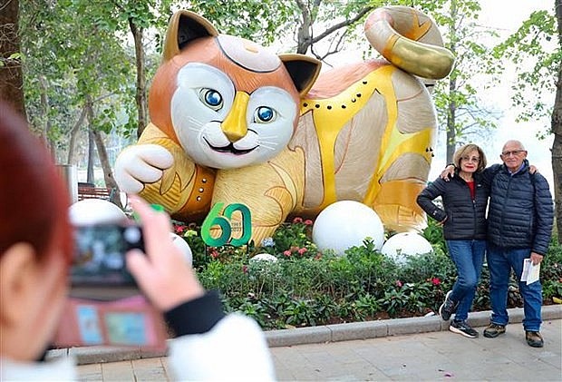 Foreign tourists pose for a photo besides a statue of the cat, the symbol of Lunar New Year 2023, in Hanoi. Photo: VNA