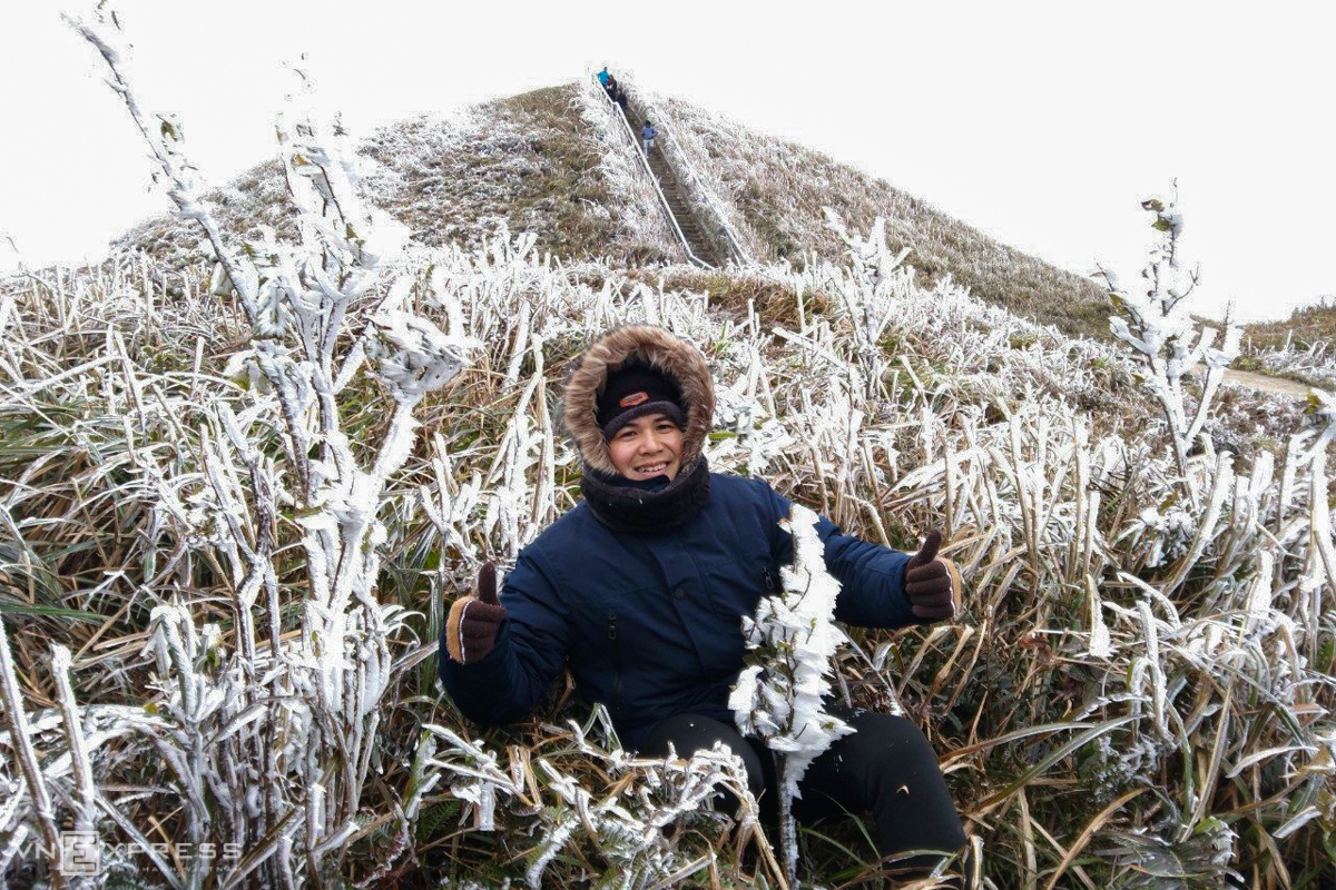 A tourist takes a check-in photo amidst the frosted grass. Given the strong cold, the man is all bundled up in a thick layer of coats (Photo: VNE) 