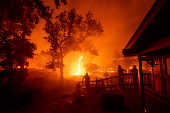 Firefighters watch flames from the LNU Lightning Complex fires approach a home in the Berryessa Estates neighborhood of unincorporated Napa County, Calif., on Friday, Aug. 21, 2020. The blaze forced thousands to flee and destroyed hundreds of homes and other structures.