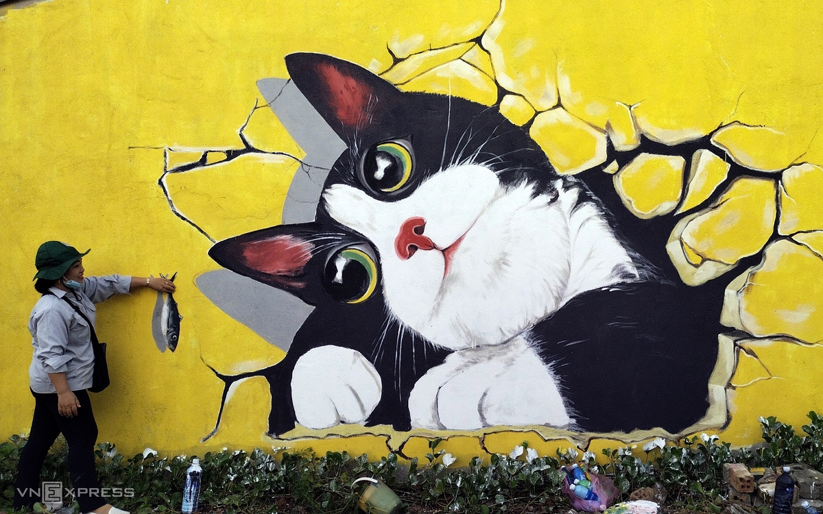 A visitor takes a picture of the hand-painting fish feeding cats on the wall.