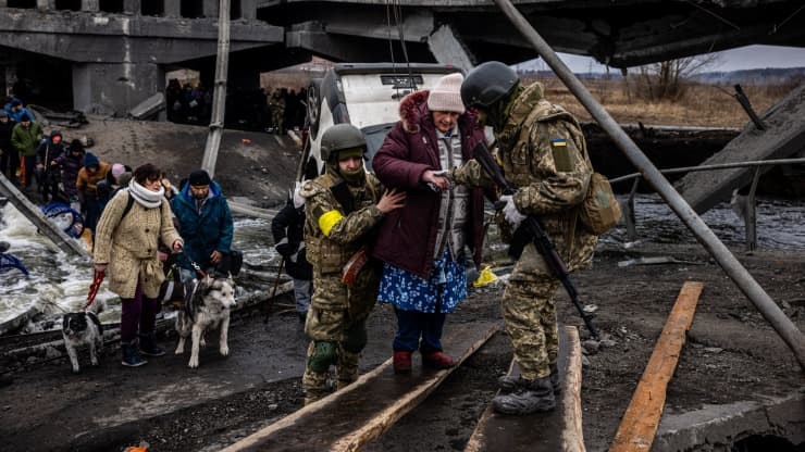 Ukrainian soldiers help an elderly woman to cross a destroyed bridge as she evacuates the city of Irpin, northwest of Kyiv, on March 7, 2022. Dimitar Dilkoff | AFP | Getty Images