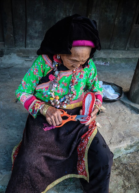 LOCAL LIVELIHOOD: An elderly Xa Phang woman making embroidered shoes outside her home. Photo laodong.vn