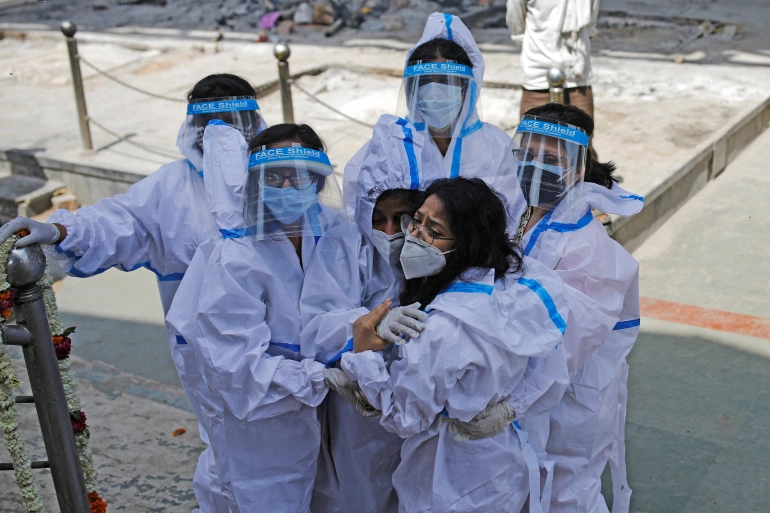 Relatives wearing personal protective equipment (PPE) mourn a man, who died from COVID-19, at a crematorium in New Delhi [Adnan Abidi/Reuters]