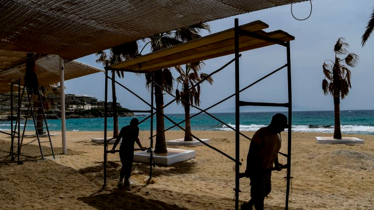 Workers carry a scaffolding on “Paradise” beach in the Greek Cycladic island of Mykonos in 2020. The island is traditionally crowded with wealthy foreigners but turned into a ghost island last year. ARIS MESSINIS | AFP | Getty Images