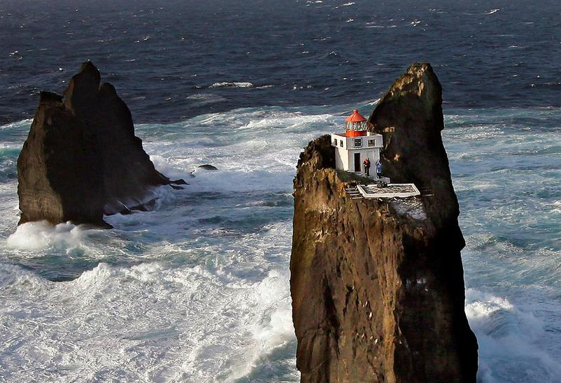 The lighthouse is surrounded by open water and is precariously perched on a cliff. Morgunblaðið/Árni Sæberg