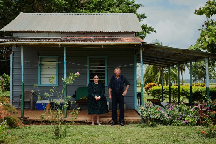 A husband and wife stand outside their home, with only the lush vegetation hinting at the photo's surprising location: Belize. Credit: Jake Michaels/Courtesy Setanta Books