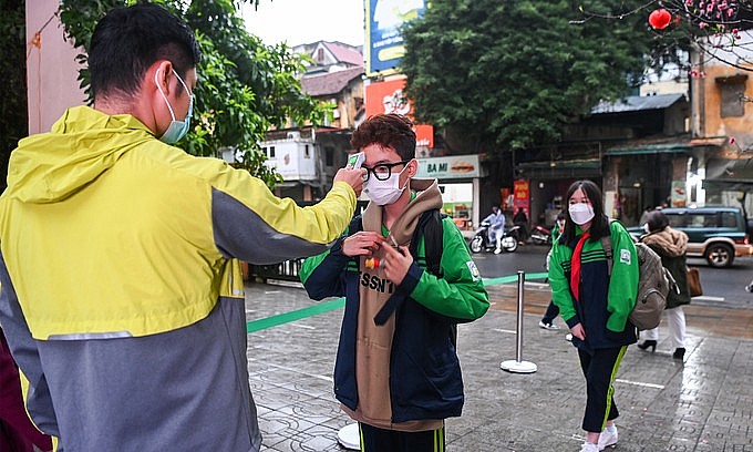 A school staff checks temperature of a student in Hanoi on February 8, 2022. Photo: VnExpress