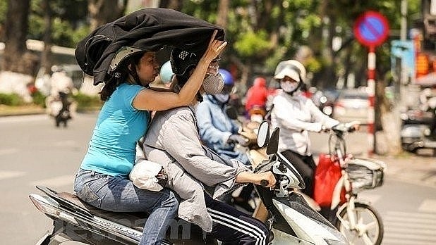Motorcylists cover themselves with thick clothing to avoid the heat. Photo: VNA