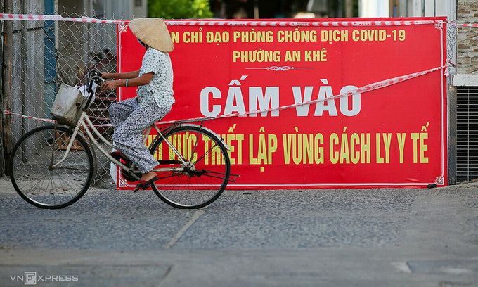 A woman cycles past a banner that indicates a locked down area due to Covid-19. Photo: VnExpress