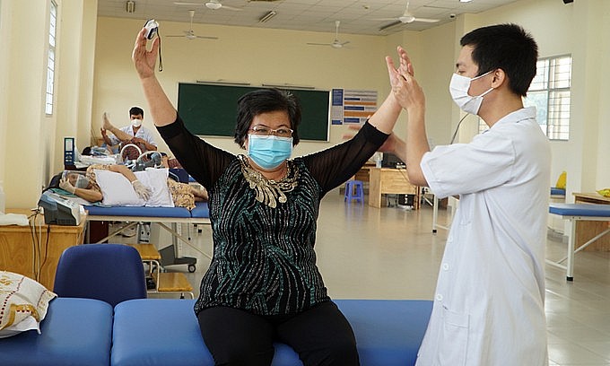 A medical worker helps a patient recovering from Covid-19 do physical exercises to improve her lung function at a hospital in HCMC, October 2021. Photo: VnExpress