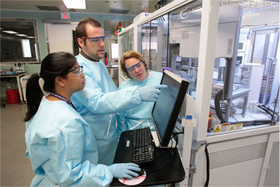 Three graduate students gather around a laboratory computer.