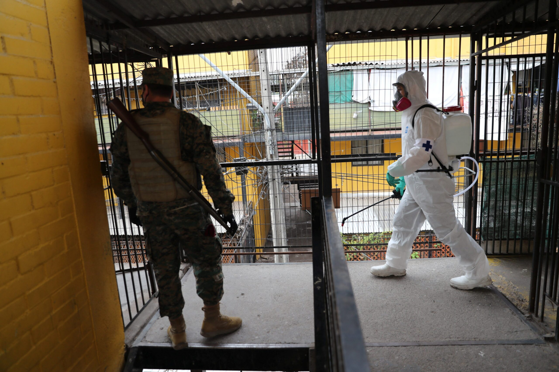 A-soldier-standing-guard-while-another-soldier-in-a-hazmat-suit-applies-disinfectant,-during-a-food-delivery-in-a-socially-vulnerable-community-in-Maipu-area-Santiago,-Chile-Photo:-Reuters
